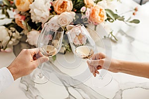 Couple on romantic date. Friends clinking glasses, top view. White wine, flowers around on marble table. Wedding celebration,