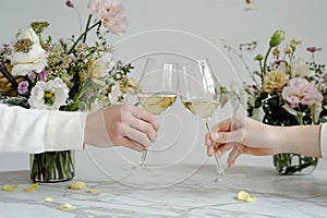 Couple on romantic date. Friends clinking glasses, top view. White wine, flowers around on marble table. Wedding celebration,
