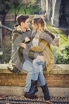 Couple with rose in love kissing on street alley celebrating Valentines day with passion sitting on city park