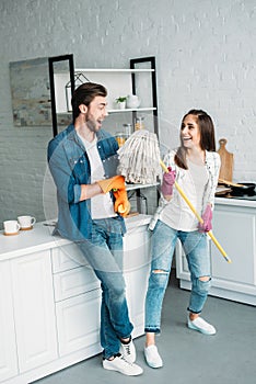 couple in rubber gloves having fun with mop in kitchen