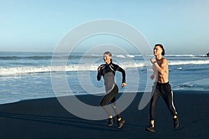 Couple Running On Beach. Handsome Man And Sexy Woman In Fashion Sporty Outfit Jogging Along Ocean Coast.