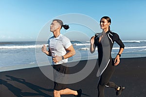 Couple Running On Beach. Handsome Man And Sexy Woman In Fashion Sporty Outfit Jogging Along Ocean Coast In Morning.