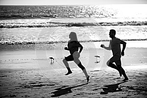 Couple running on beach. Silhouette of young man and woman running jogging along the sea.