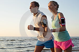 Couple running on the beach during sunset with their headphones plugged in