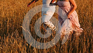 Couple running in a grassy field, the woman wearing a long, flowing dress.