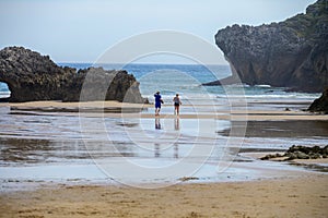 Couple running on Playa de Palombina Las Camaras in Celorio, Green coast of Asturias, North Spain with sandy beaches, cliffs, photo