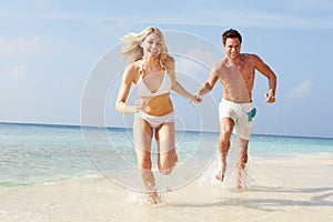 Couple Running Through Waves On Beach Holiday