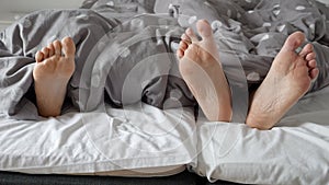 Couple's feet showing from under the blanket while cuddling in bed. The concept of intimacy, togetherness.
