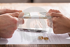 Couple`s Hand Holding Currency Over The Divorce Agreement