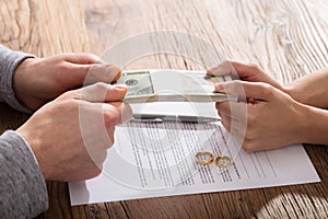 Couple`s Hand Holding Currency Over The Divorce Agreement