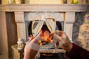 Couple`s hands with glass of champagne near fireplace