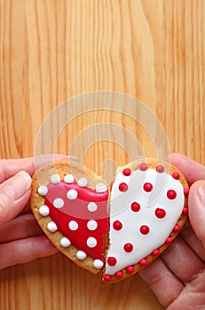 Couple`s hands holding two half heart shaped cookies attach on wooden background