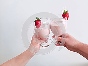 Couple`s hands holding up glasses with strawberry buttermilk cocktail.