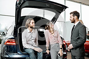 Couple with salesperson on the back of a new car in the showroom