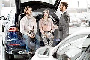 Couple with salesperson on the back of a new car in the showroom