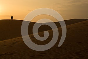 Couple on sand dune in desert , sunset sky