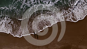 Couple on a sandy beach by the sea. Two are standing by the sea. Top view drone shot. Travel concept