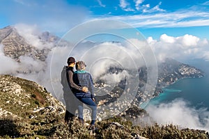 Couple with scenic view from Monte Comune on clouds covering the coastal town Positano at the Amalfi Coast, Campania, Italy.