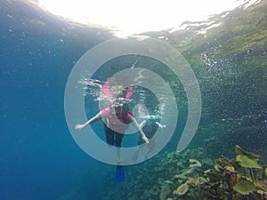 Couple scuba diving under crystal clear water with tank, fins and visor happy swim and share their love doing exercise and living