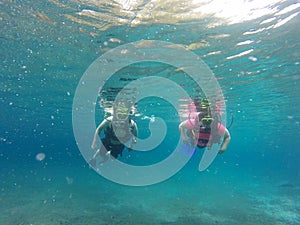 Couple scuba diving under crystal clear water with tank, fins and visor happy swim and share their love doing exercise and living