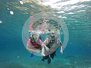 Couple scuba diving under crystal clear water with tank, fins and visor happy swim and share their love doing exercise and living