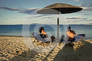 Couple secrets fantasy. Couple in love at sea resort sits on loungers under umbrella on sand beach. Couple on vacation