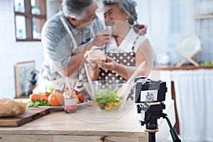 Couple senior Asian elder happy living in home kitchen. Grandfather wiping grandmother mouth after eating bread with jam vlog vdo