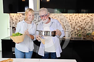 Couple senior caucasian husband and wife in casual dress standing, cooking salad with relaxation in kitchen at house. Happy