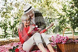 Couple senior man surprise giving gift box to his wife while relaxing in the park