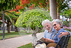 Couple of senior people  relax on a bench in public park reading a book - happy retirement concept with retired couple together