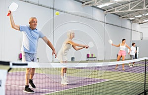 Couple of senior woman and man playing doubles pickleball indoors