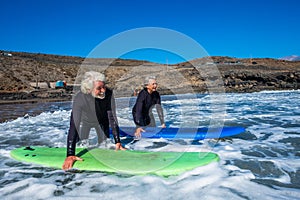 Couple of seniors at the beach with black wetsuits holding a surftable ready to go surfing a the beach - active mature and retired