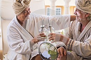 Couple of seniors in a beauty house together taking a cocktail sitting  with cream on the face of the mature man - two pensioners