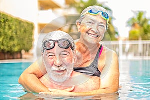 Couple of seniors enjoying summer and having fun together in the pool swimming and smiling looking at the camera - cheerful happy