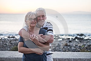 Couple of seniors hogging at the beach with a lot of love - retired together - woman with glasses and man with sea background