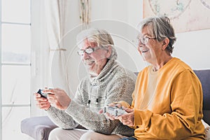 Couple of seniors and mature people looking and the tv and using controllers playing video games at home together on the sofa -