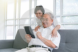 Couple of seniors smiling and looking at the same tablet hugged on the sofa