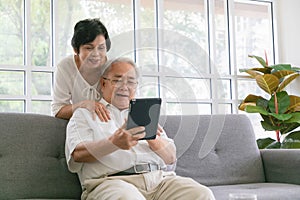 Couple of seniors smiling and looking at the same tablet hugged on the sofa