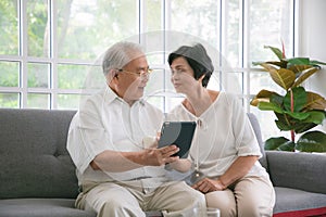 Couple of seniors smiling and looking at the same tablet on the sofa