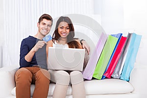 Couple shopping online with bags on sofa