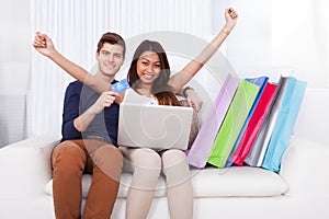 Couple Shopping Online With Bags On Sofa