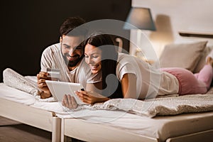 Couple shopping online from the comfort of bedroom and using digital tablet and credit card