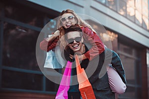 Couple in shopping together. Happy couple shopping together and having fun. Boyfriend carrying his girlfriend on the piggyback.