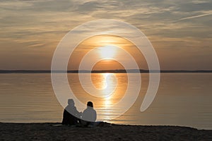 Couple on the shore of the lake during summer sunset and beautiful evening sky. Romance, love, relationships, friendship