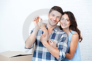 Couple showing keys to new home hugging looking at camera