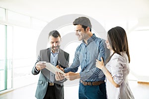 Couple Signing Agreement By Real Estate Agent In New Apartment