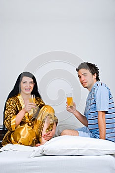 Couple sit on bed drinking orange juice