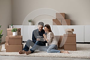 Couple sit on floor near boxes use tablet discuss purchase