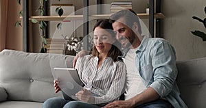 Couple sit on sofa making video call using digital tablet