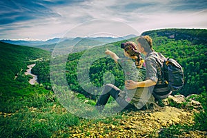 Couple sits on the edge and looks to the mountains, girl points, the effect of the retro camera